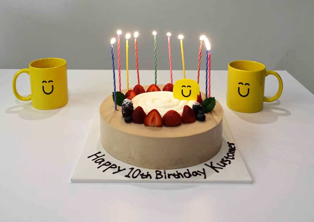 Image of a cake with 10 candles that says Happy 10th birthday Kustomer on a white table