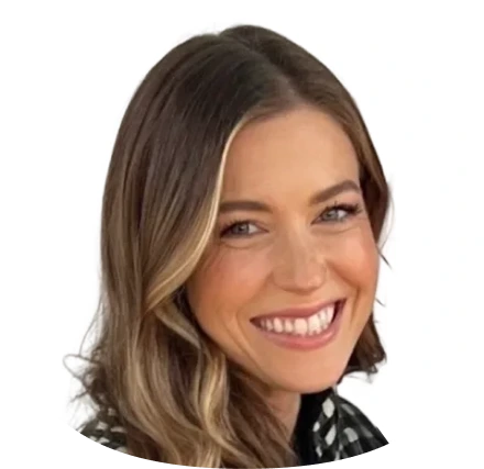 A woman with long blonde hair is smiling at the camera. She is wearing a dark top, and the background is plain white.