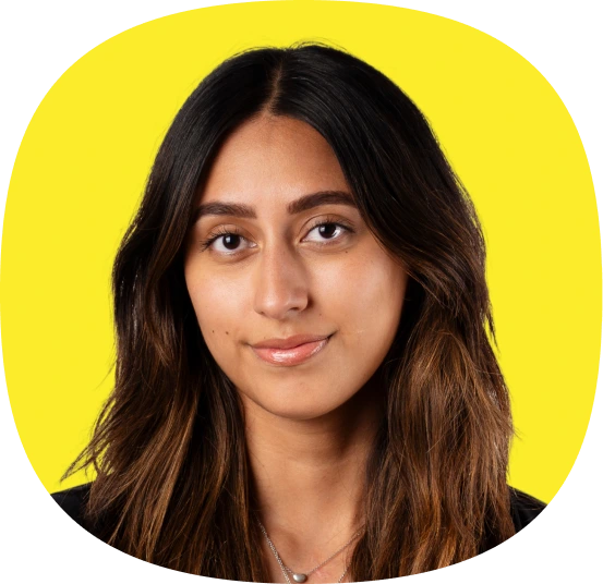 A woman with long, dark hair and a slight smile poses in front of a bright yellow background. She is wearing a black top and a necklace.