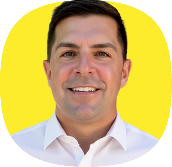 A man with short dark hair, wearing a white collared shirt, smiles at the camera against a bright yellow background at a Kustomer customer experience leader event.