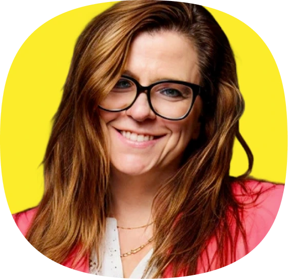 A smiling woman with long brown hair, wearing black glasses, a pink blazer, and a white top, posed in front of a bright yellow background at a Kustomer customer experience leader event.